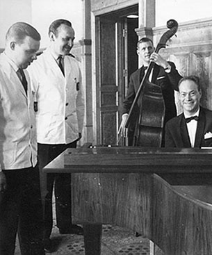 Stadhotellets nyinvigning 1959. Servitörerna Nils Sundberg och Stig Vikström står i vita serveringsrockar och ser Bengt Hallberg vid pianot. Basist i bakgrunden.